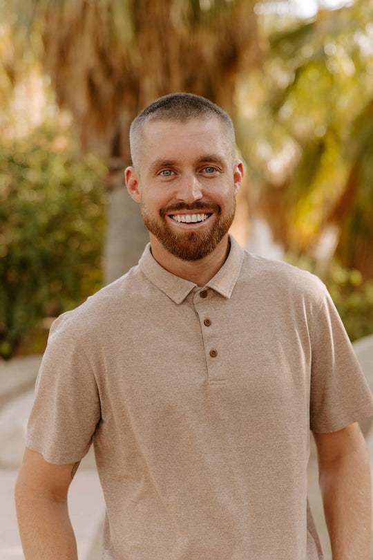 A smiling Mark Miller real estate agent in a polo shirt, standing outdoors with a Desert background.