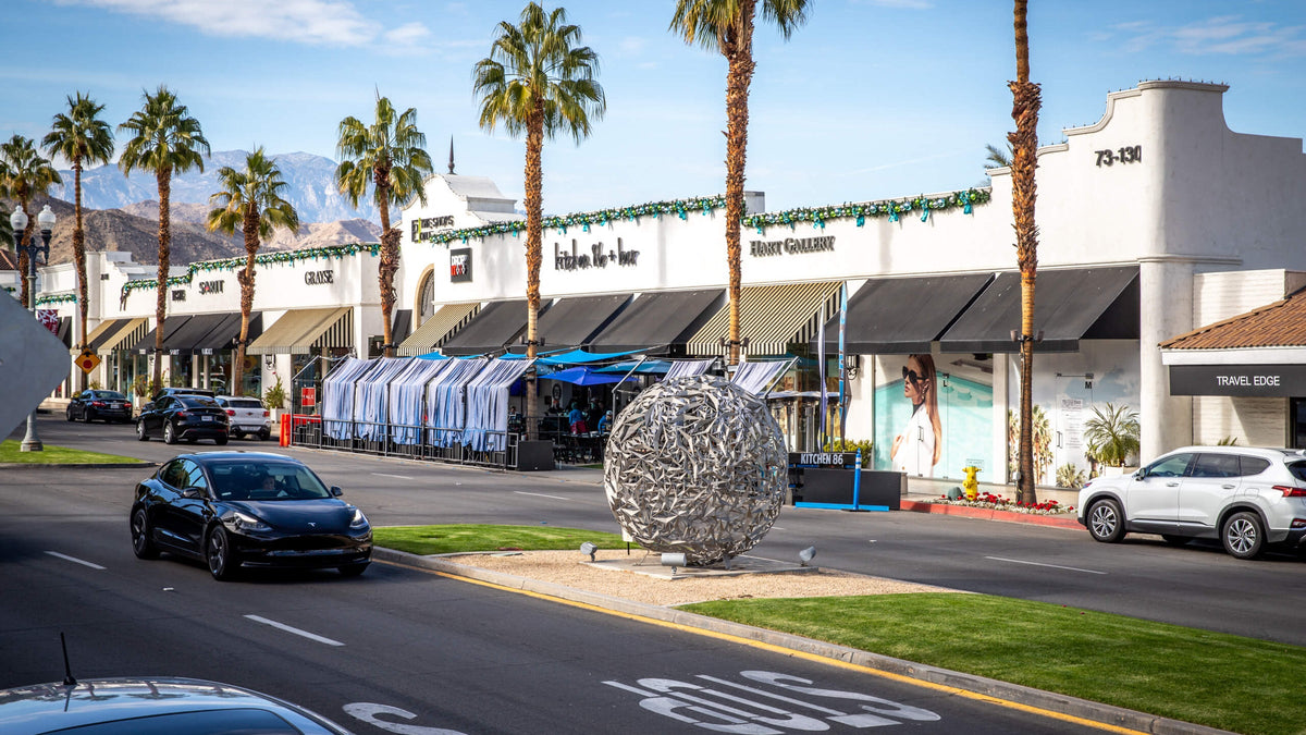 Outdoor sculpture, palm trees, and white storefronts along El Paseo in Palm Desert, photographed by Mark Miller in 2021.