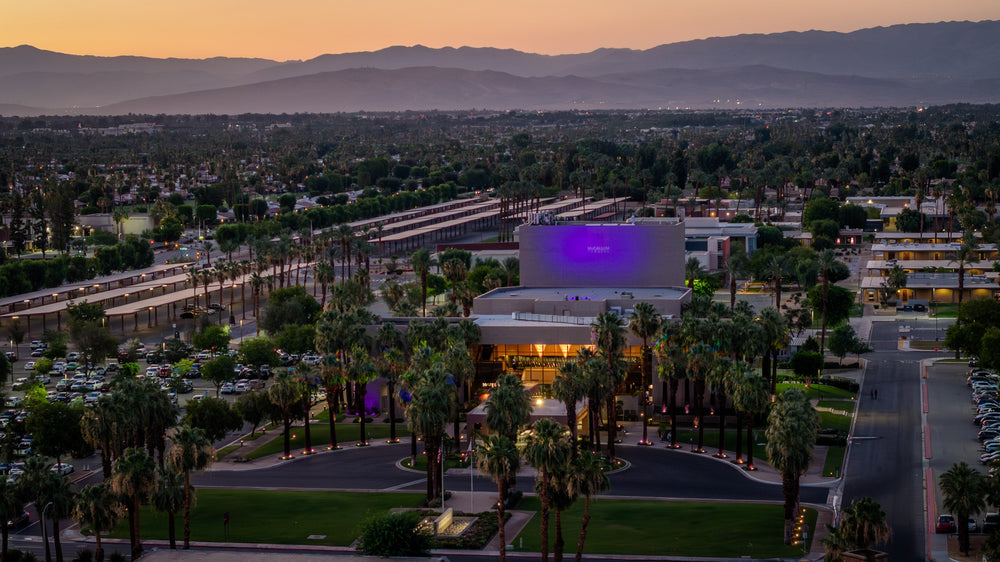 McCallum Theatre at sunset in Palm Desert with palm trees, city lights and the Santa Rosa Mountains