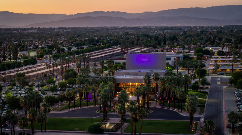 McCallum Theatre at sunset in Palm Desert with palm trees, city lights and the Santa Rosa Mountains