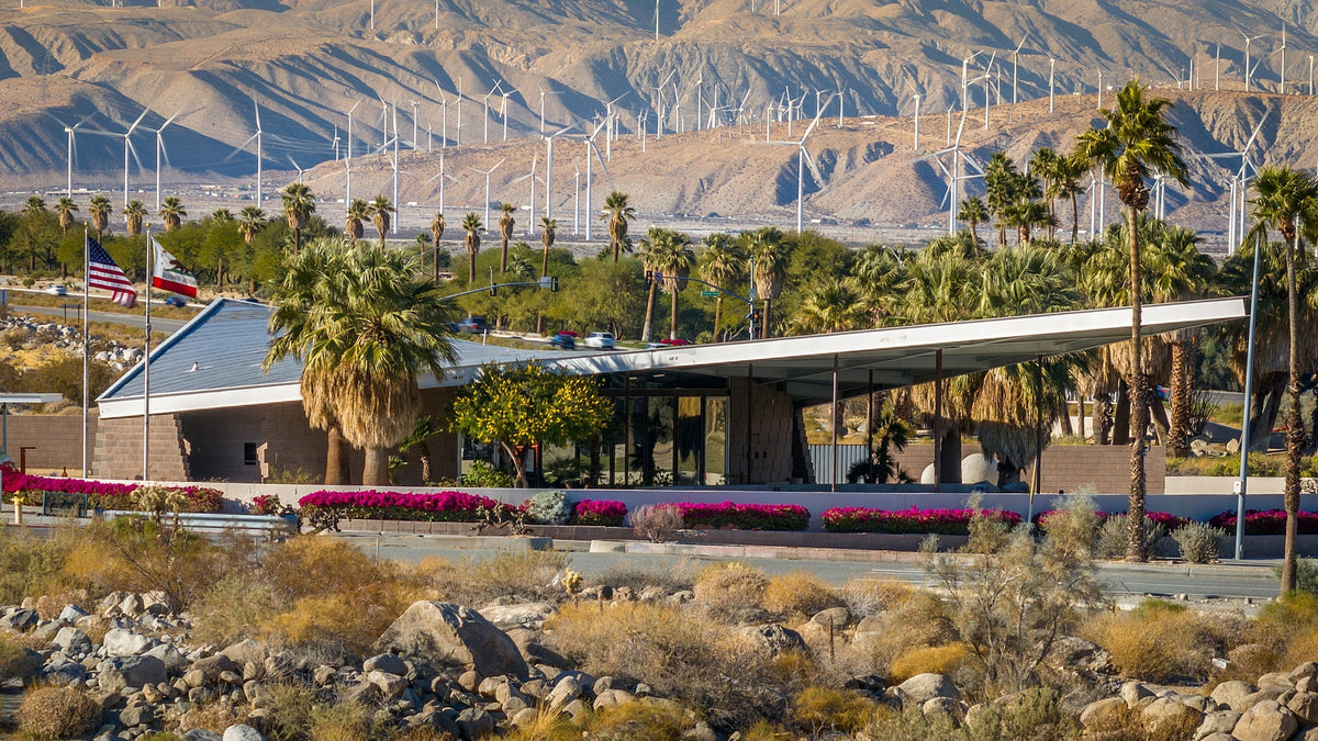 Palm Springs Visitor Center with palms, wind turbines, and desert mountains behind it