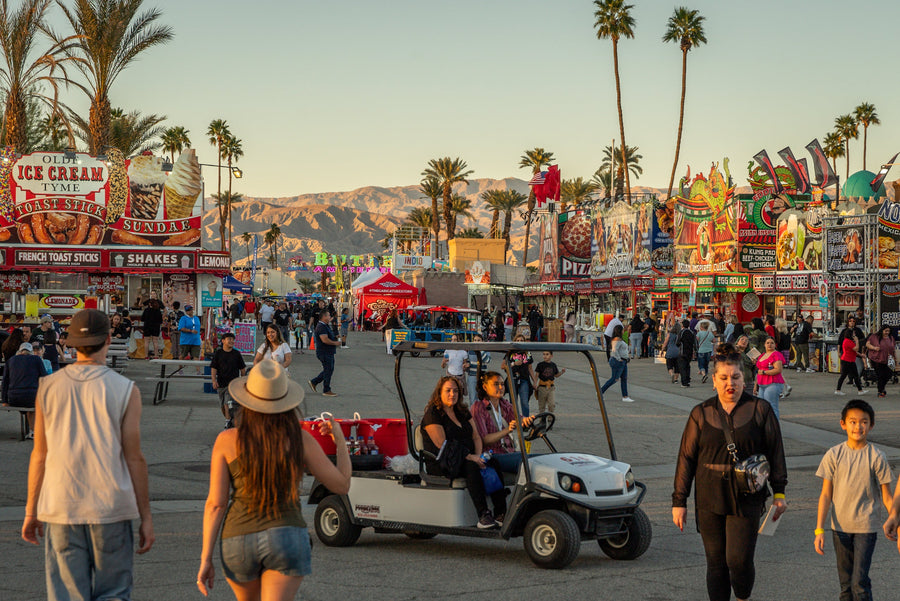 Visitors fill the Date Festival midway beneath palms and mountains at sunset in Indio
