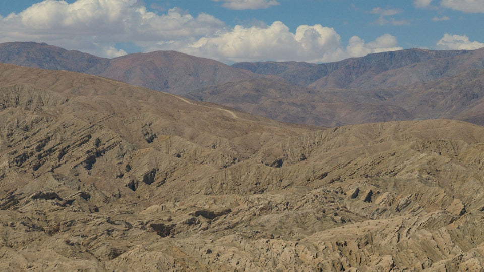 Panoramic view of layered, eroded Indio Hills beneath white clouds near the San Andreas fault zone. Photograph by Mark Miller.
