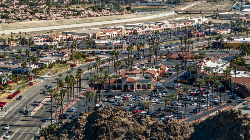 Elevated view of Highway 111 in La Quinta, with shopping centers, palm trees, and the desert ridge in the foreground.