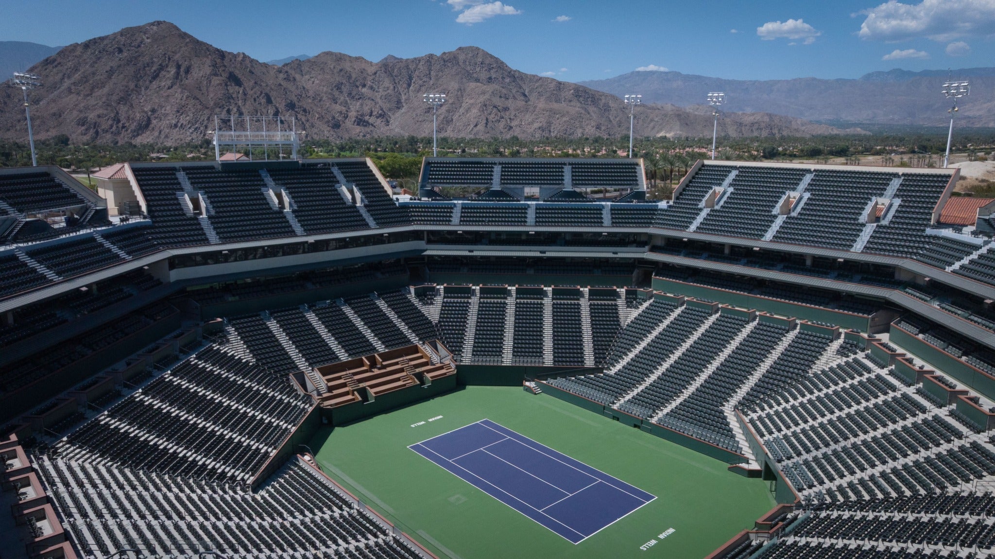 Empty Stadium 1 court at the Indian Wells Tennis Garden with the Santa Rosa Mountains rising beyond the upper seats.