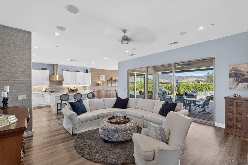 Open-concept living room and kitchen in a Trilogy Polo Club home, with sliding glass doors opening to a furnished patio and mountain views.