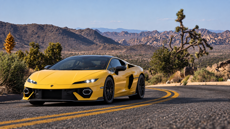 Yellow Lamborghini driving along a winding road in Joshua Tree, surrounded by desert mountains and Joshua trees.