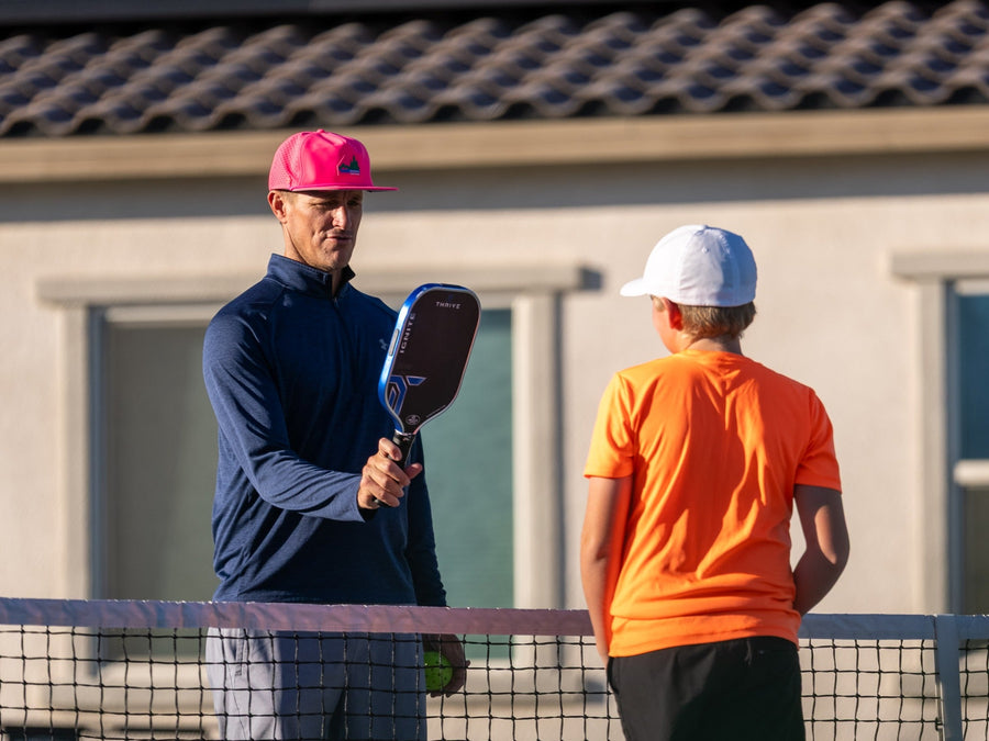 Matt Anderson holding his pickleball paddle while coaching a student in an orange shirt in La Quinta. Photo by Mark Miller.