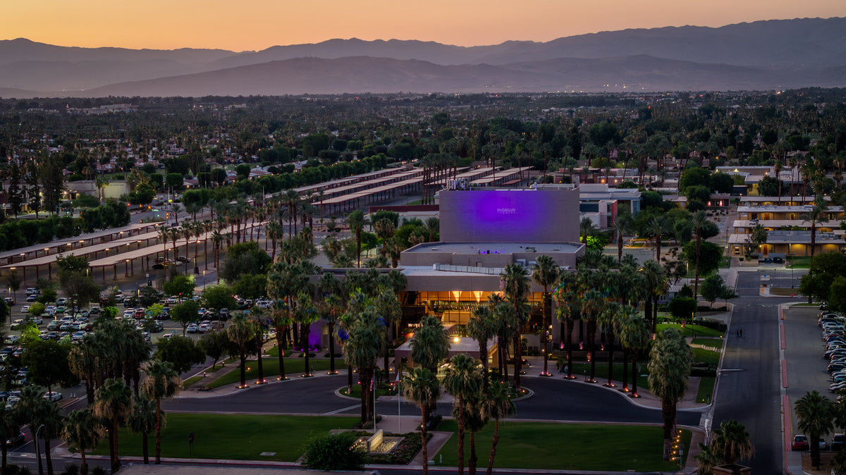 McCallum Theatre in Palm Desert, California at sunset with palm trees, city lights, and mountain views