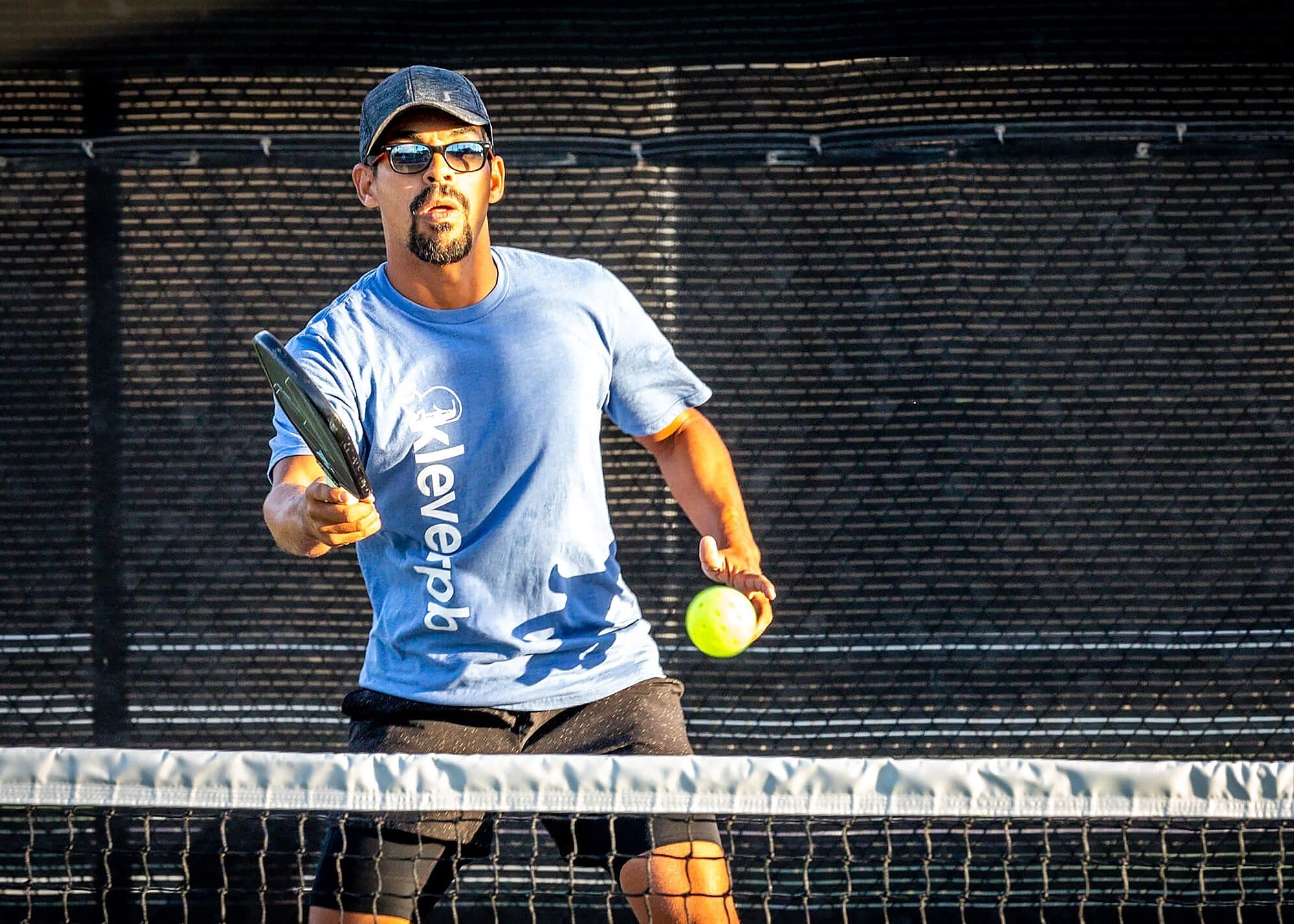 Pickleball player holding a paddle and ball at the net