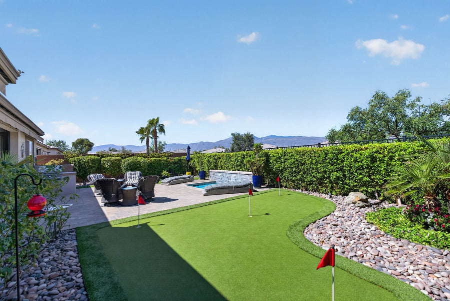 Trilogy Polo Club backyard with a putting green, paved seating patio, small pool, hedges, and mountain views.