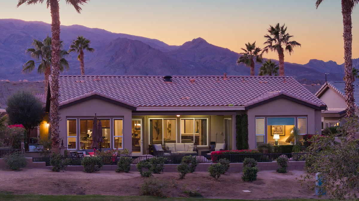 Evening view of a residential house in Trilogy La Quinta with palm trees in the foreground and mountains in the background.