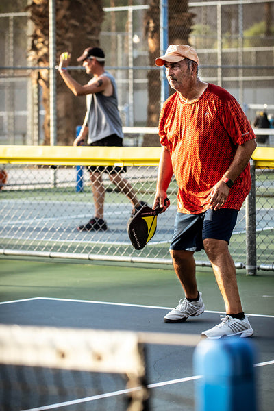 Man playing pickleball on an outdoor court with another player in the background.