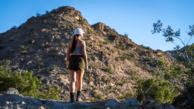 Woman standing on a rocky desert path looking up at a mountain in La Quinta, California under a blue sky.
