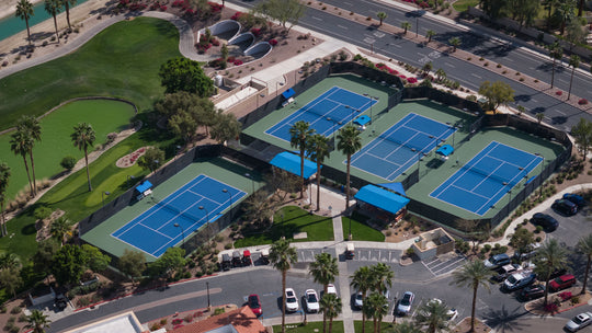 Aerial view of a tennis complex with multiple blue courts surrounded by greenery and parking lots at the Montecito Clubhouse in sun city shadow hills ca