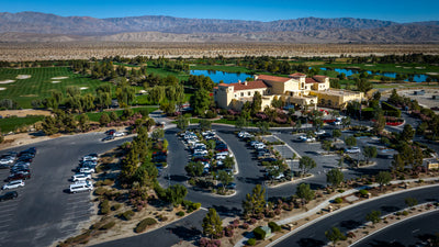 Wide aerial view of The Classic Club clubhouse, golf course and ponds beneath desert mountains.
