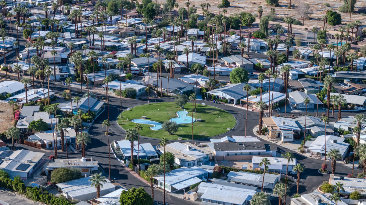 Aerial view of Blue Skies Village in Rancho Mirage, showing its central landscaped green, curving streets, low-rise homes and tall palms; photographed by Mark Miller on October 13, 2026