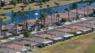 Duna La Quinta homes beside a palm-lined street, lake and fountain