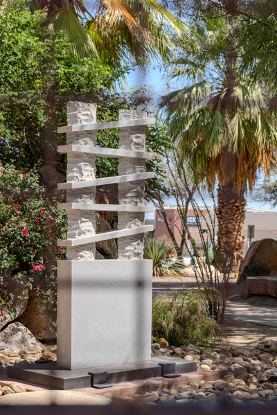 Reflective geometric sculpture on a rectangular pedestal among palms at Faye Sarkowsky Sculpture Garden.