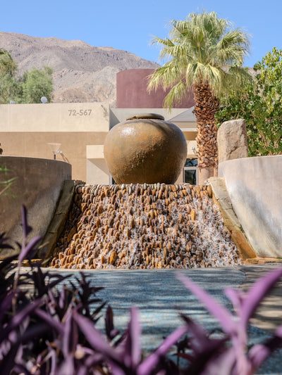 Large urn above a cascading fountain framed by palms and mountains at Faye Sarkowsky Sculpture Garden.