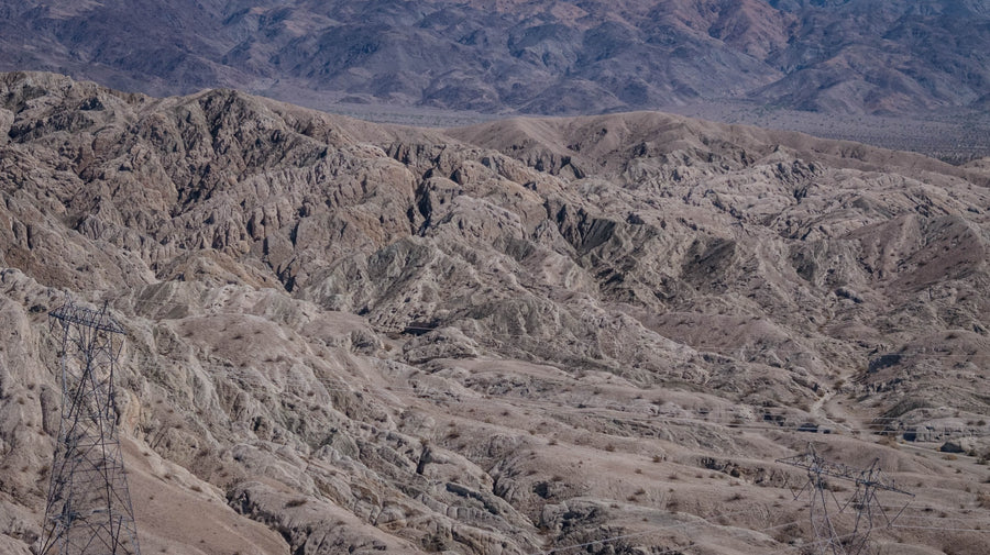 Sculpted Indio Hills badlands with transmission towers and desert mountains beyond, photographed by Mark Miller on September 29, 2026.