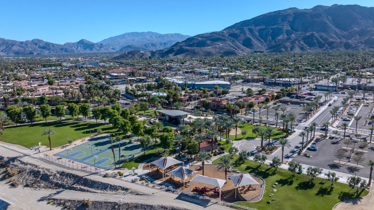 Aerial view of Rancho Mirage Community Park, with shaded playgrounds, basketball courts, lawns and mountains beyond.