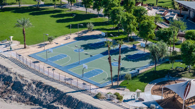 Two blue and green basketball courts at Rancho Mirage Community Park beside open lawns and palm trees.
