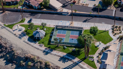 Two fenced pickleball courts beside a picnic shelter, lawn and walking paths at Rancho Mirage Community Park.