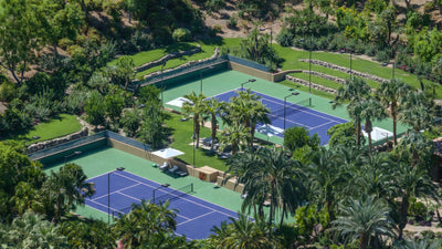 Blue and green tennis courts enclosed by hedges and palm trees at Sensei Porcupine Creek.