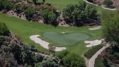 Close elevated view of a golf green, white sand bunkers and flowering landscaping at Sensei Porcupine Creek.