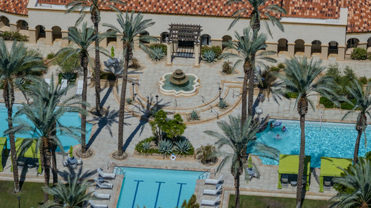 Close aerial view of The Regent Palm Desert's clubhouse entrance, fountain, pool terrace and palm trees. Photo by Mark Miller, September 10, 2026.